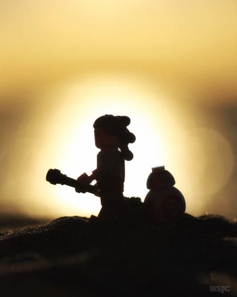 A lego Rey and BB8 walk across the sand with the setting sun leaving them in full relief.
