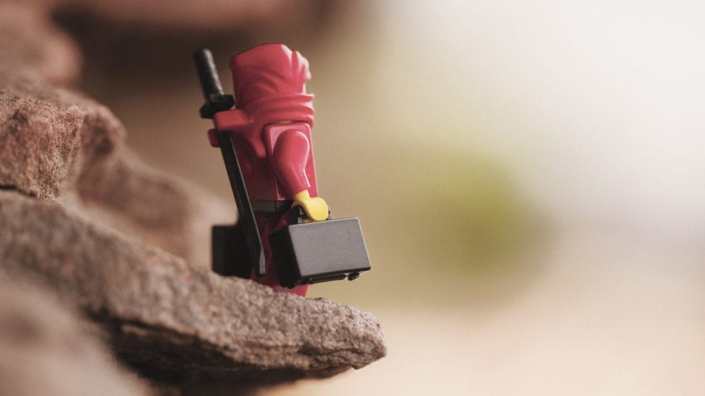 A Lego Ninja stands on the edge of a cliff holding two suitcases wondering where he should go.